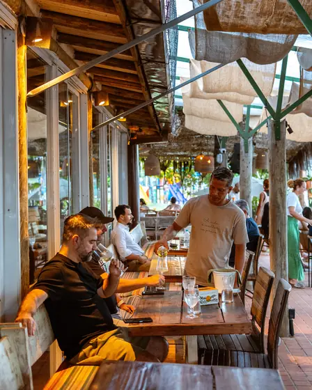Clientes no deck coberto do Clericot, com o garçom servindo a mesa