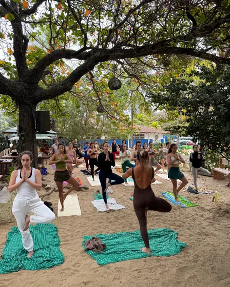 Turma de yoga na postura da árvore, na areia do Clericot